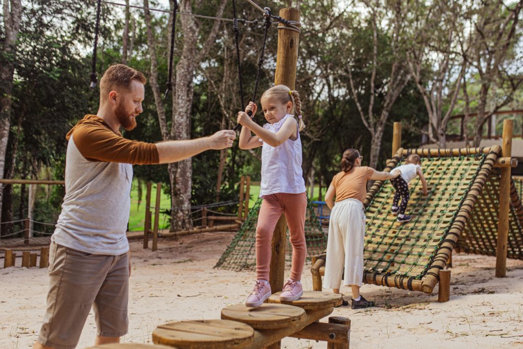 Pai e mãe brincando com as filhas em um parquinho.